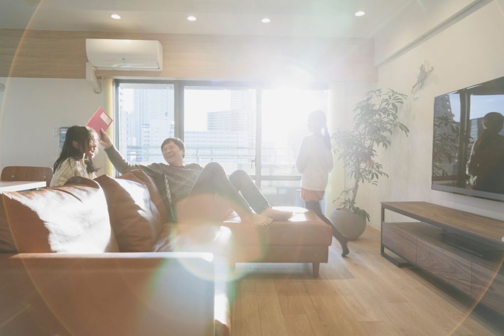 A family of four sitting together on a couch in a cozy living room, surrounded by warm lighting and decorative elements.