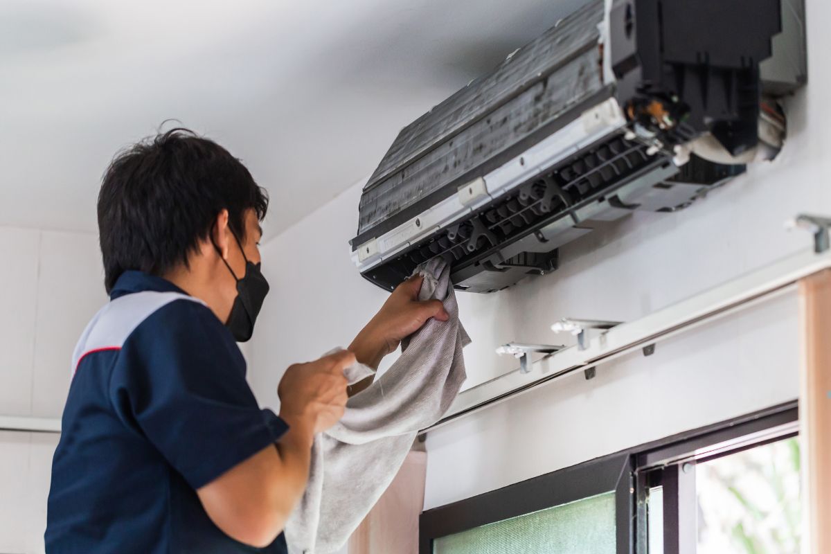 A man diligently cleaning an air conditioning unit with a cloth in a well-lit room.